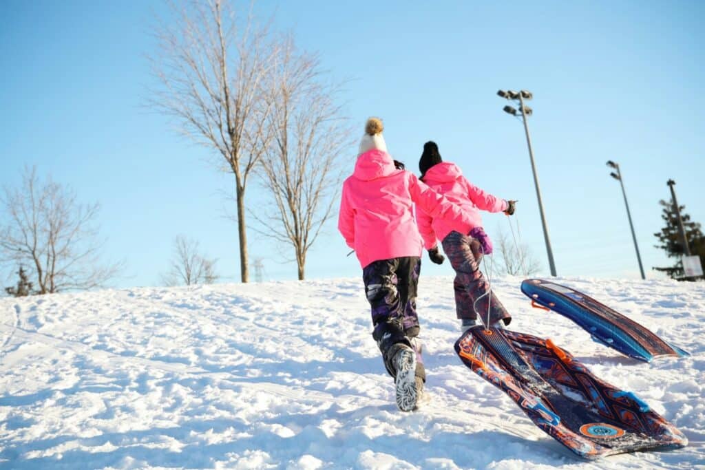 people hiking up snow covered hill with sleds